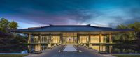 a building that is made out of wood and surrounded by water at dusk with the moon rising behind it