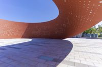 a large red sculpture sits next to some bricks in a square area with lots of holes