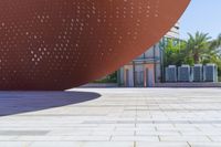 an orange sculpture on a sidewalk outside of a building with white dots on it,