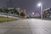 a city with skyscrapers at night with a light post in the foreground and a walkway lined with green grass