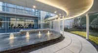 a circular garden at the entrance to an office building with many windows and lights above