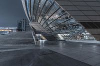 view of the outside of a glass building and staircase at night in europe on a dark, cloudy day