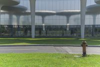 an old fire hydrant in the middle of a grassy park near a building with glass doors