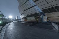 a stone walkway in a plaza next to a tall building at night with an outside patio area