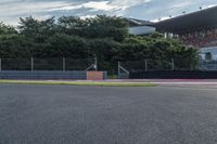 the motorcycle is driving next to the gate on the track, near the grass and trees