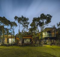 a night time photo of several cabins in a field with trees and bushes, surrounded by some grass, and wooden steps