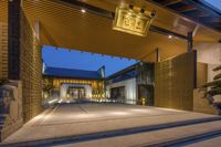 an entrance is shown at dusk and has a wooden ceiling with lighting, plants and a sign above