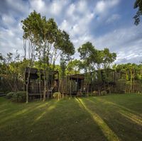 the house is surrounded by trees and green grass near the road side fence and walkway