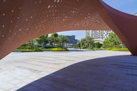 an artisticly designed city square has a bright pink canopy and fountain for children in the center