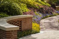 a brick and stone wall lined with flowers and plants, along with a walkway and a bench