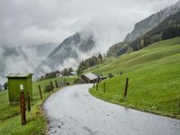 a view of a wet road in the countryside during the day time, with low clouds