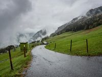 a view of a wet road in the countryside during the day time, with low clouds