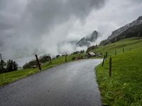 a view of a wet road in the countryside during the day time, with low clouds
