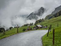 a view of a wet road in the countryside during the day time, with low clouds