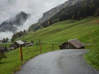 a view of a wet road in the countryside during the day time, with low clouds
