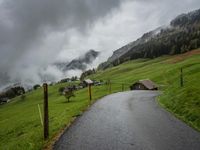 a view of a wet road in the countryside during the day time, with low clouds