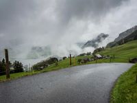 a view of a wet road in the countryside during the day time, with low clouds