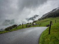 a view of a wet road in the countryside during the day time, with low clouds