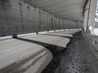 a very long sidewalk that is by some concrete buildings with a roof over it that has concrete walls