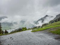a view of a wet road in the countryside during the day time, with low clouds