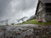 a view of a wet road in the countryside during the day time, with low clouds