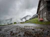 a view of a wet road in the countryside during the day time, with low clouds