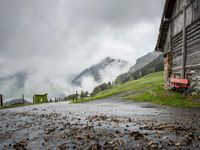 a view of a wet road in the countryside during the day time, with low clouds