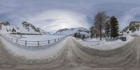 snow covered mountains and buildings surround a road that runs between the fences in a snow - covered landscape