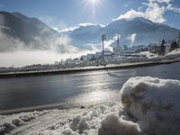 the view of snow piled up next to a road in front of mountains and snow covered city