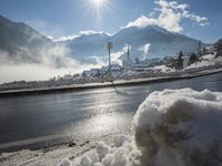 the view of snow piled up next to a road in front of mountains and snow covered city