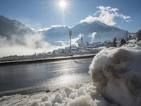 the view of snow piled up next to a road in front of mountains and snow covered city