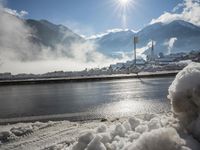 the view of snow piled up next to a road in front of mountains and snow covered city