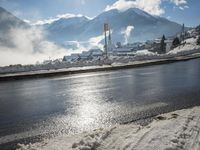 the view of snow piled up next to a road in front of mountains and snow covered city