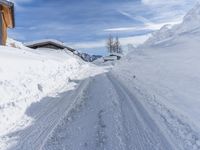 a snowy road covered in a lot of snow next to a house and mountains and trees