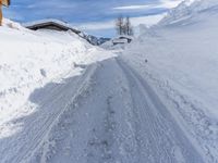 a snowy road covered in a lot of snow next to a house and mountains and trees
