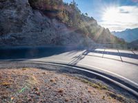 a truck driving down a highway in front of a cliff covered hillside area with the sun in between the hills