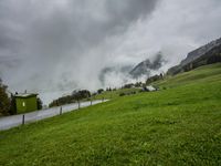 a view of a wet road in the countryside during the day time, with low clouds