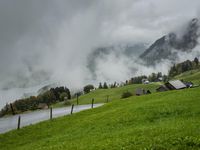a view of a wet road in the countryside during the day time, with low clouds