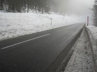 a snowy street with trees and a white fence near by, foggy scene, winter