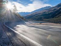 road next to a mountain under a cloudless sky with the sun coming down in the middle