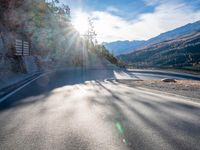 road next to a mountain under a cloudless sky with the sun coming down in the middle