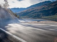 road next to a mountain under a cloudless sky with the sun coming down in the middle