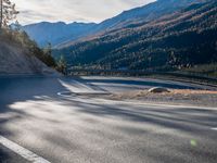 road next to a mountain under a cloudless sky with the sun coming down in the middle