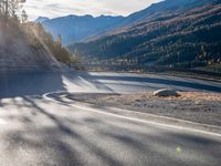 road next to a mountain under a cloudless sky with the sun coming down in the middle