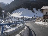 a view from the side of a long mountain road in a town with snow covered mountains