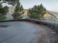 there is a stone path next to a winding mountain side road with some trees in the foreground