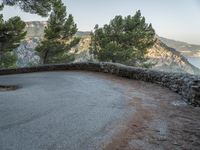 there is a stone path next to a winding mountain side road with some trees in the foreground