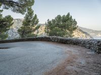 there is a stone path next to a winding mountain side road with some trees in the foreground