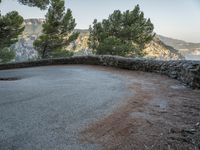 there is a stone path next to a winding mountain side road with some trees in the foreground