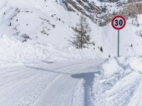 the speed limit sign is on the side of the snow covered road, near the snow - filled mountain